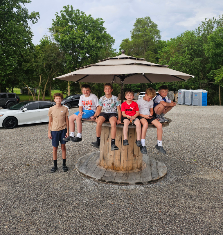 Seven boys sitting on wooden spool under umbrella